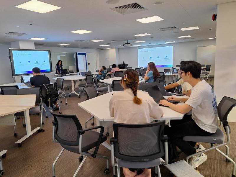 Students attend a data science workshop in a modern classroom, seated at tables with laptops while a presenter speaks beside slides titled "Why Use Data Science?"